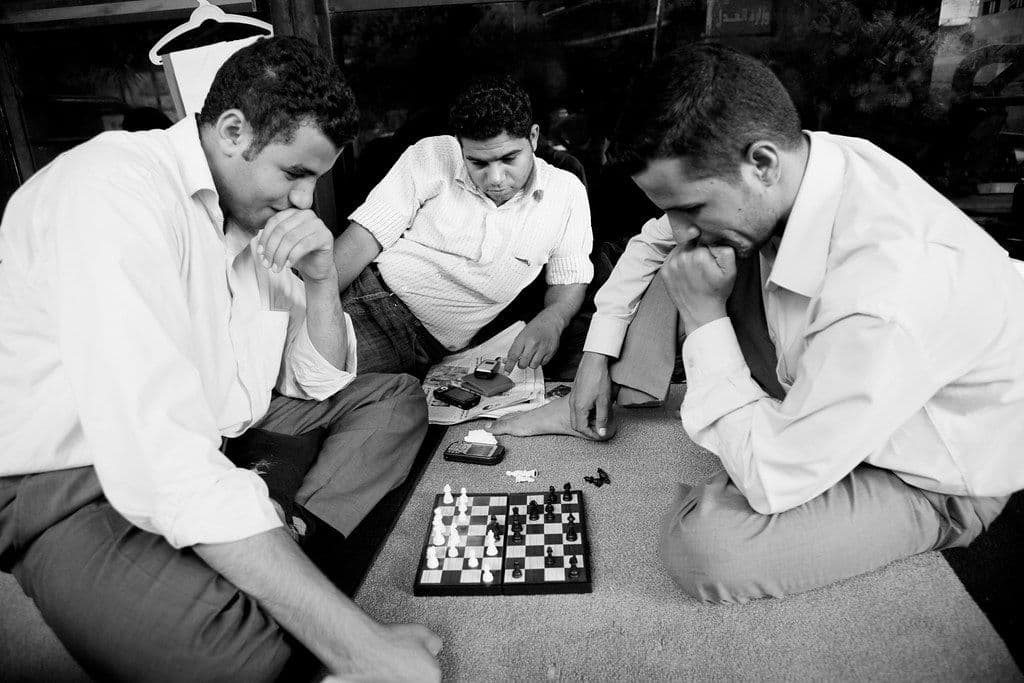 Three men playing chess on the ground at a street corner in Egypt