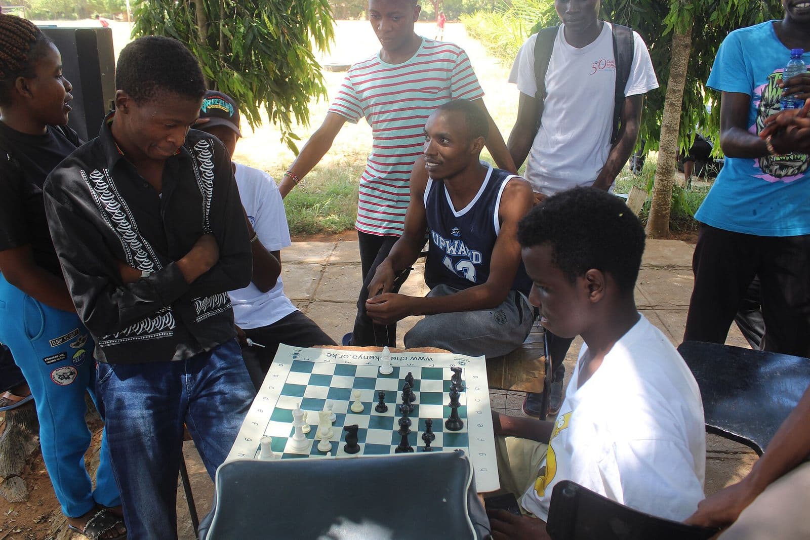 A crowd of young players gathered around an outdoor board in Kilifi, Kenya