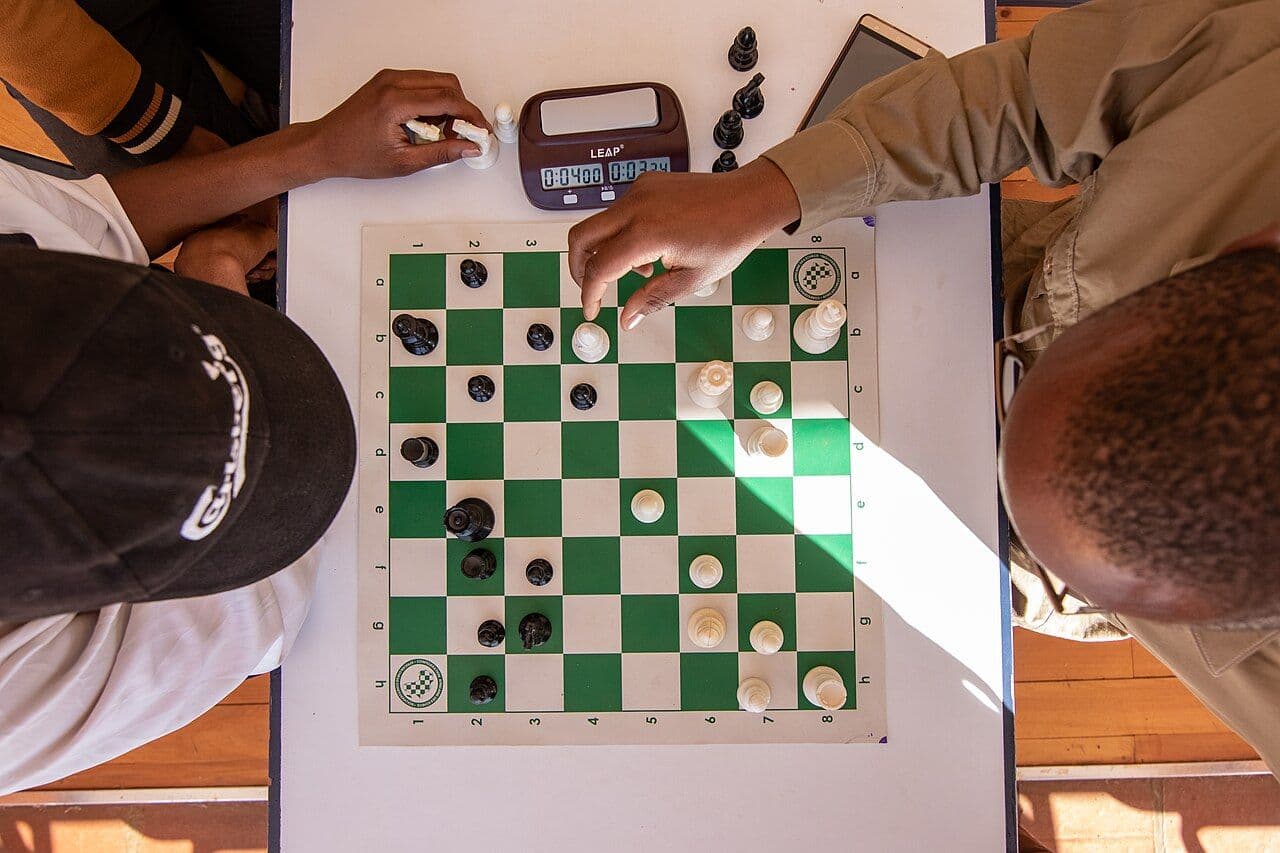 Two players over a green board with a clock, seen from directly above